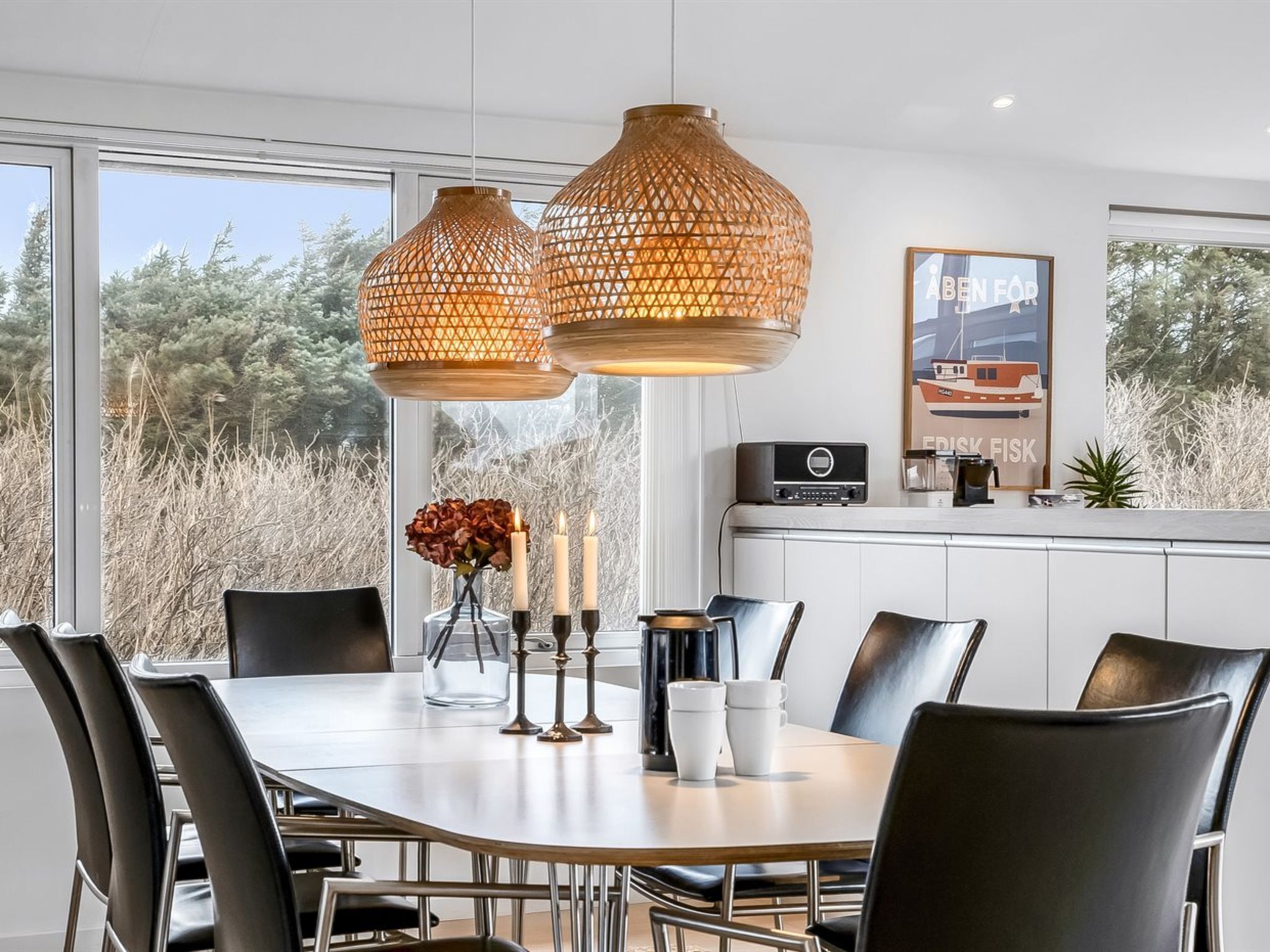 A modern dining area with a large table, black chairs, and two hanging pendant lights.