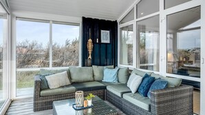 Una sala de estar moderna con un sofá seccional, una mesa de centro de vidrio y ventanas amplias con vistas al exterior.