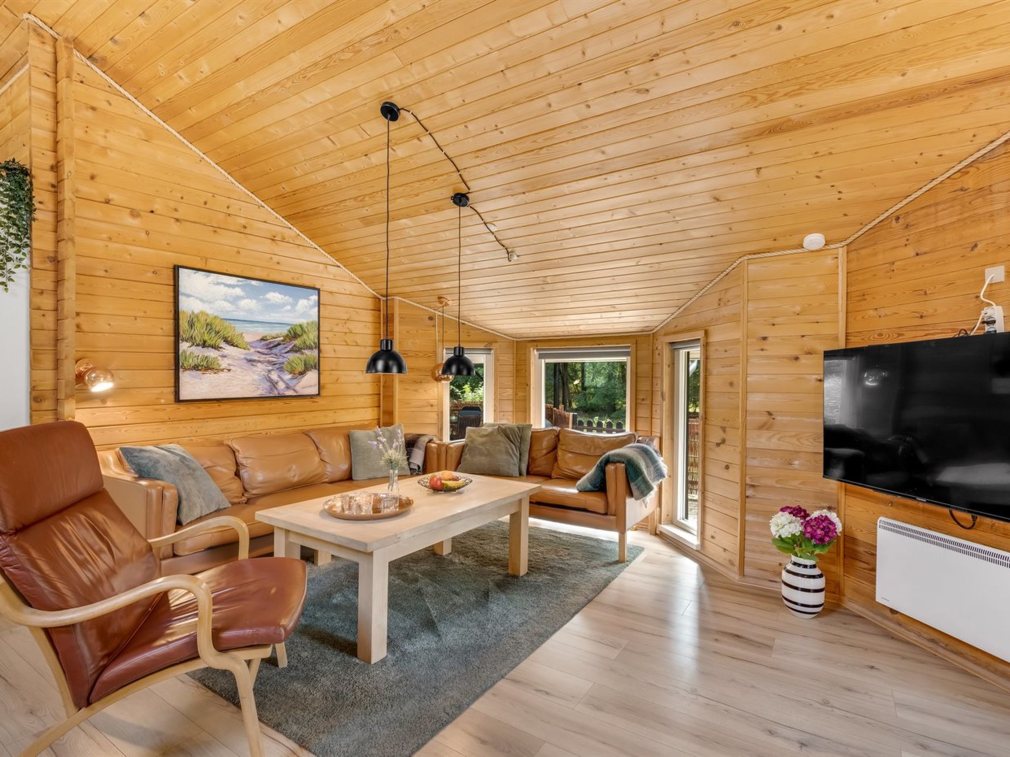 Een gezellig houten interieur met een plafond, een bank, een eettafel en een televisie.
