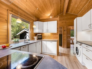 A modern kitchen with wooden walls, white cabinets, a built-in stove, and a washing machine. - "Jorina" - 700m to the fjord by Interhome (Ringkøbing)
