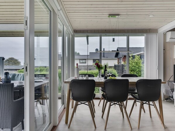 A modern dining area with a table set for four, large windows offering a view of the neighborhood, and a ceiling with a light fixture.