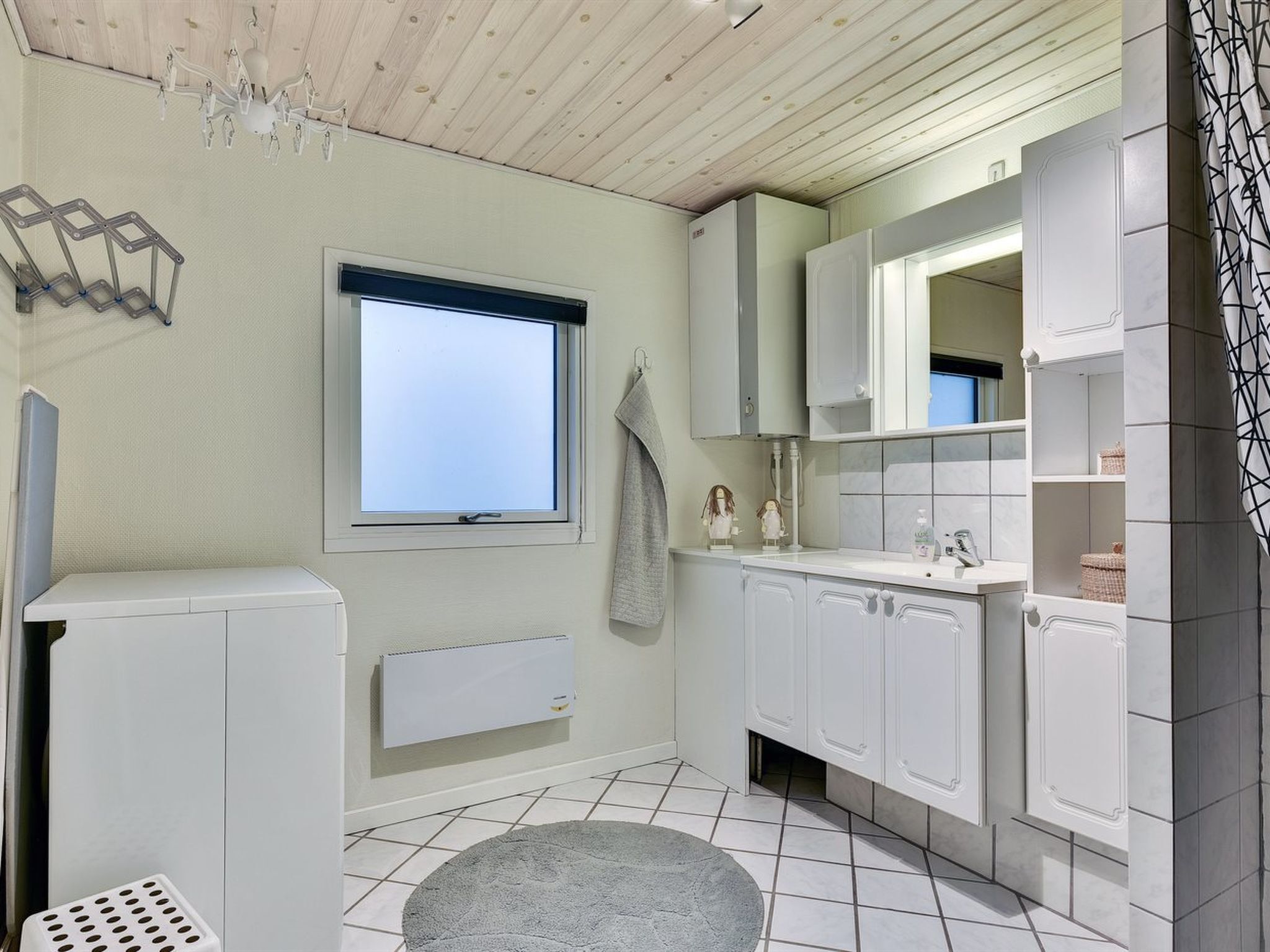 A modern bathroom with white cabinetry, a built-in window, a radiator, and a grey rug on the floor.