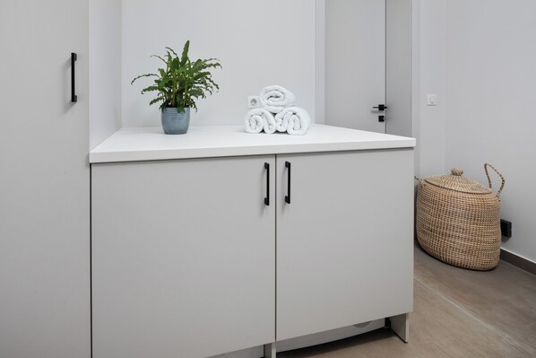 A white cabinet with black handles, a potted plant, and rolled towels on top. - Luxurious Villa with seafront view and infinity pool (Mparmpati)