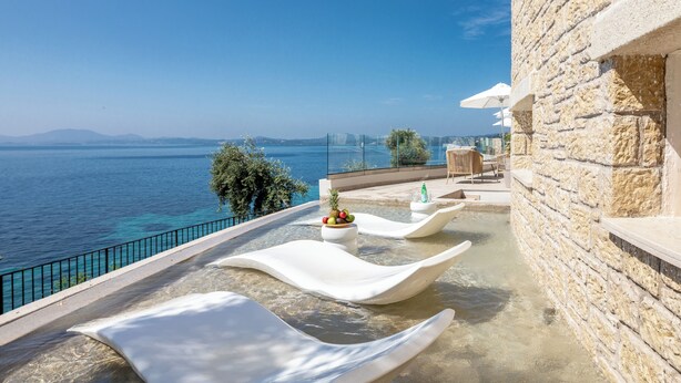 Un balcón con vista al mar, un muro de piedra y una zona de estar con mesa y sillas.