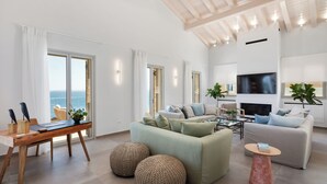 Amplia sala de estar con sofá, mesa de centro y chimenea. Cuenta con un comedor con mesa y sillas, y grandes ventanales con vistas al mar.