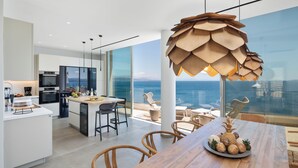 Una cocina moderna con una isla grande, un comedor con mesa de madera y vistas al océano.