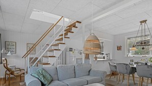 Ein modernes Wohnzimmer mit einem grauen Sofa, einem kleinen runden Tisch, einer Treppe mit Holzstufen und einer Pendelleuchte.