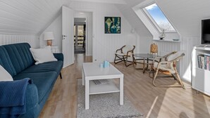 Ein modernes Loft mit hohen Decken, weißen Wänden, einem blauen Sofa, einem weißen Couchtisch, Korbstühlen und einem Oberlicht.