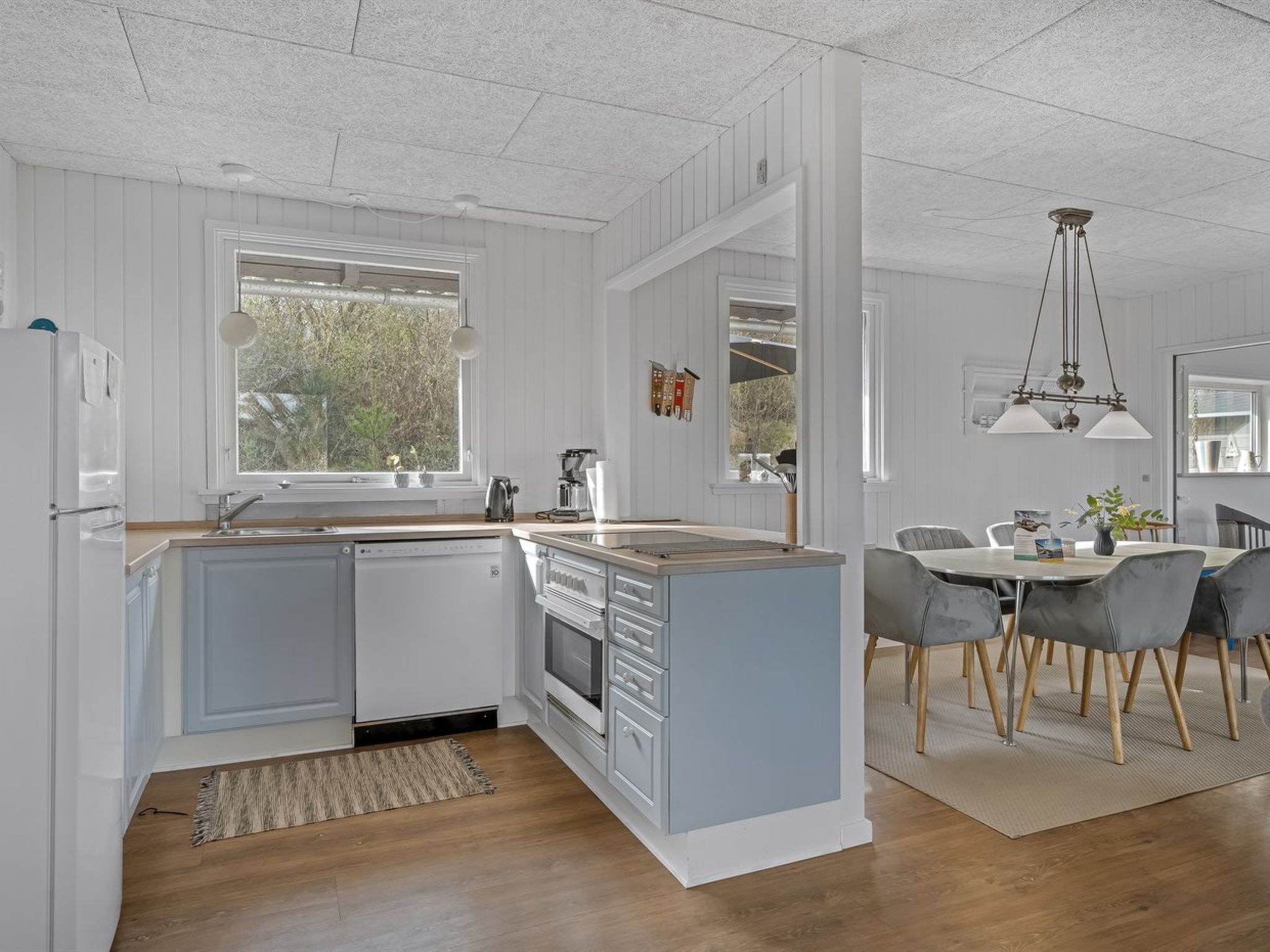 Une cuisine moderne avec des meubles blancs, un lave-vaisselle encastré et un coin repas comprenant une table et des chaises.