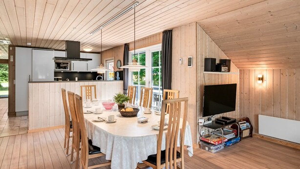 Una cocina moderna con una isla central, mesa de comedor de madera con sillas y un televisor de pantalla plana.
