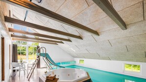 Una piscina interior moderna con tobogán, jacuzzi y zona de estar con vistas al exterior.