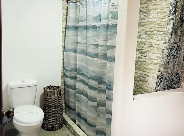 Un baño con inodoro, una cesta de mimbre y una cortina de ducha con estampado de olas.