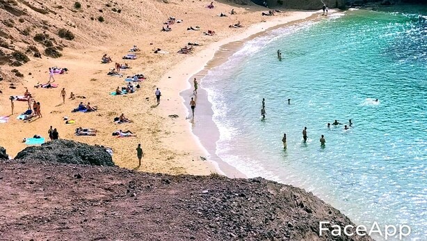 Une plage où des gens se prélassent au soleil et se baignent, entourée de falaises rocheuses.