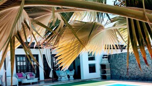 Un espace aménagé au bord de la piscine, avec des chaises longues, un mur en pierre et un bâtiment aux grandes fenêtres en arrière-plan.
