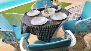 Un espace extérieur aménagé pour les repas, avec une piscine, des chaises et une table préparée pour deux personnes.