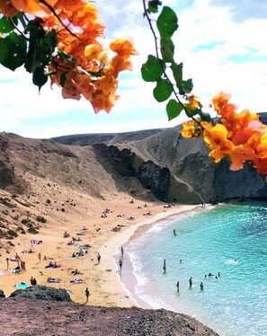 Una playa con gente tomando el sol y nadando, rodeada de acantilados rocosos.