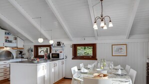 A modern kitchen with white cabinetry, a central island, and a dining area with a table set for six. - "Hildegarda" - 1km from the sea by Interhome (Sæby)