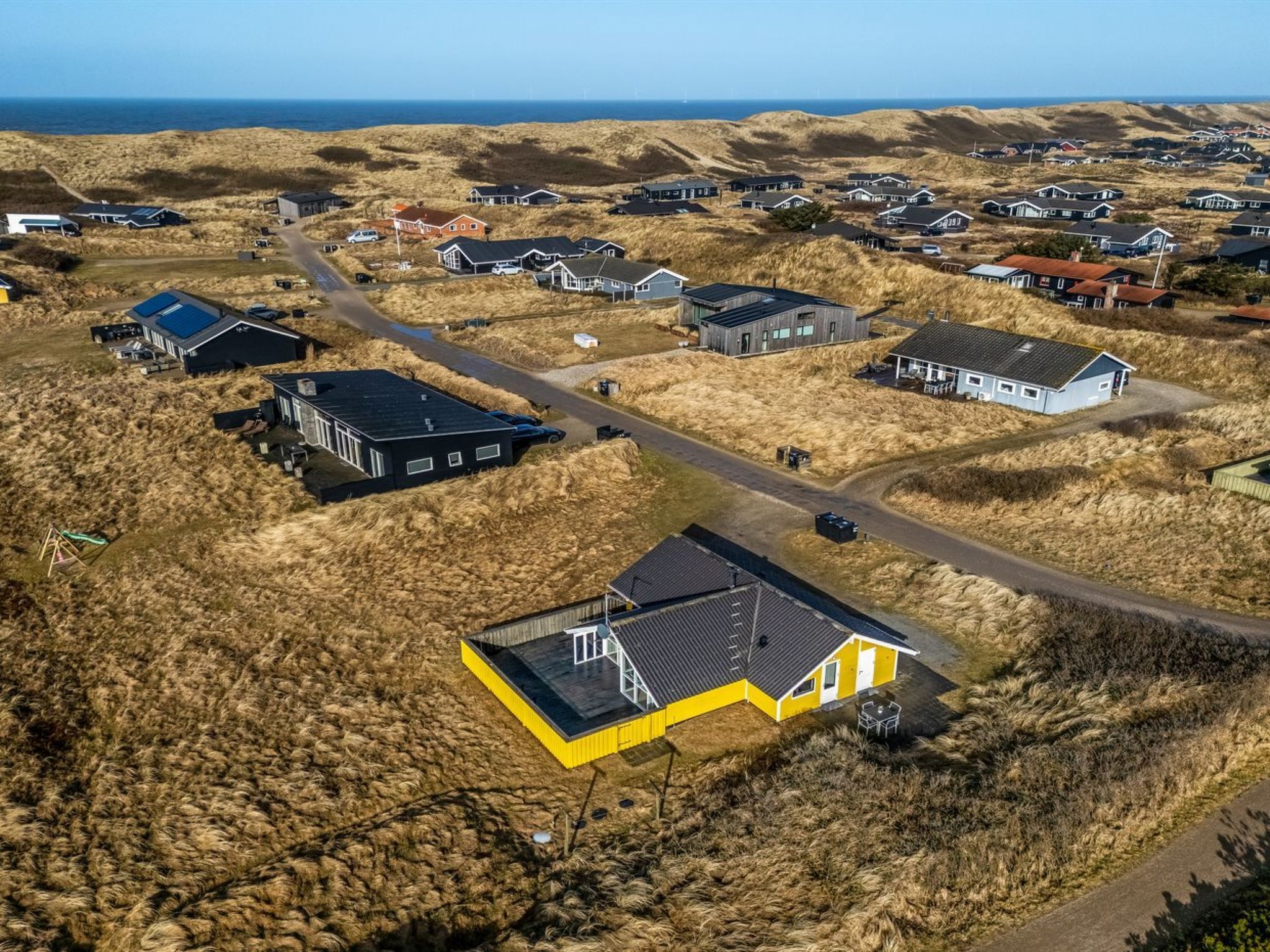 Vue aérienne d’une zone résidentielle côtière, avec des maisons, des routes et une plage.