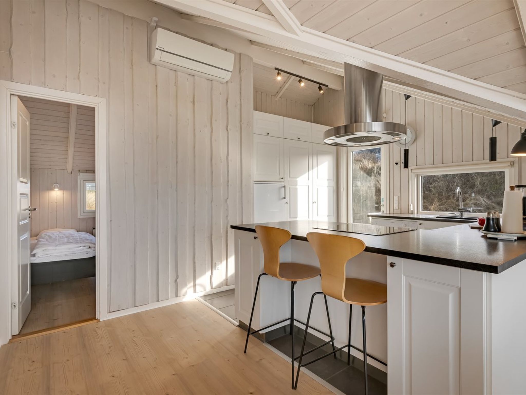 A modern kitchen with white cabinetry, a stainless steel range hood, and two bar stools.