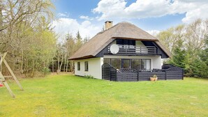Et hus med stråtækt tag og balkon, omgivet af en velplejet græsplæne og træer.
