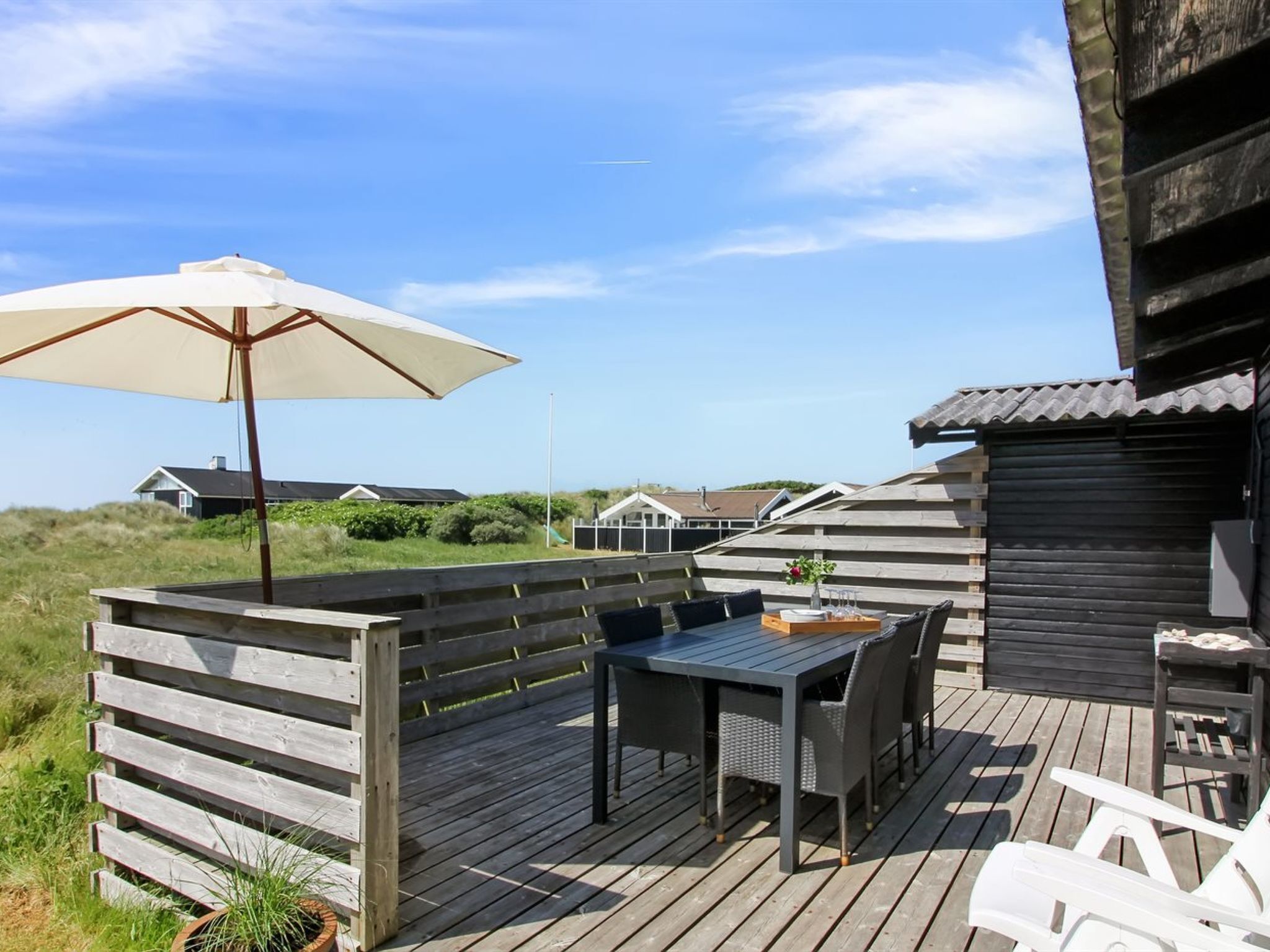 Eine Holzterrasse mit Tisch und Stühlen, einem großen Sonnenschirm und Blick auf die umliegende Landschaft.