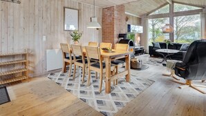Een ruime woonkamer met een houten vloer, een eettafel met stoelen, een open haard en een groot raam dat voor natuurlijk licht zorgt.