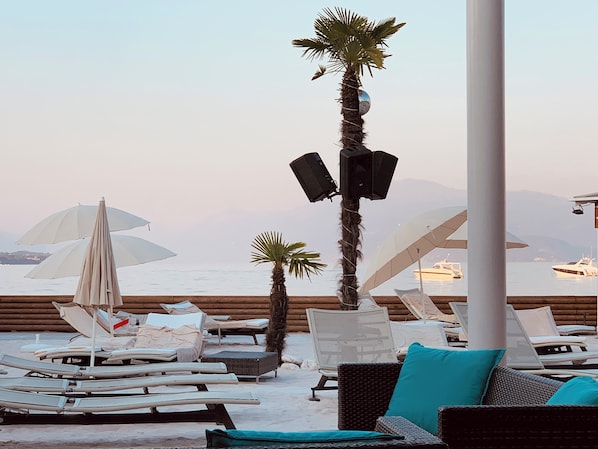 A beachside lounge with sun loungers, umbrellas, and a palm tree.
