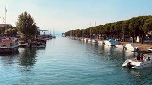 A marina with boats docked along the water's edge, surrounded by trees and a clear sky. - Fantastically beautiful ambience on 93sqm in Peschiera, 5 min=lake 7min=center, balcony (Peschiera del Garda)