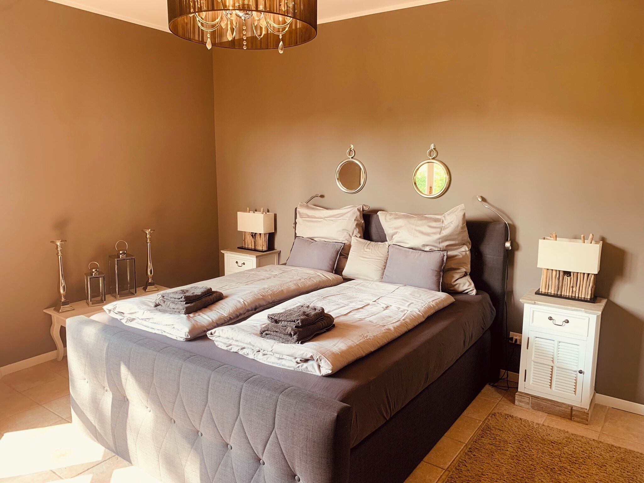 Ein Schlafzimmer mit einem großen Bett, zwei Nachttischen, einer Chandelüster und einem Beistelltisch mit einer Lampe.