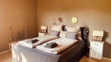 Une chambre à coucher avec un grand lit, deux tables de chevet, un lustre et une petite table de nuit avec une lampe.