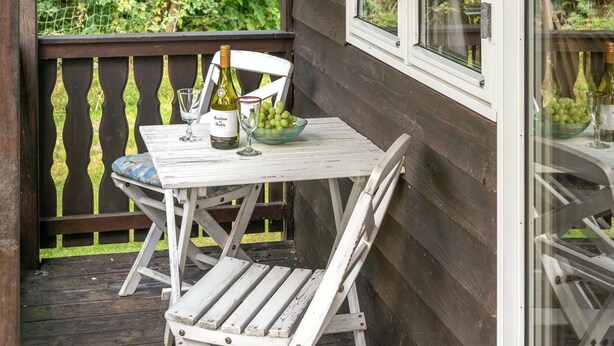 Eine Holzterrasse mit einem weißen Tisch und Stühlen, einer Weinflasche und einer Schüssel mit Trauben.