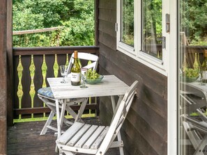 A wooden deck with a white table and chairs, a bottle of wine, and a bowl of grapes.