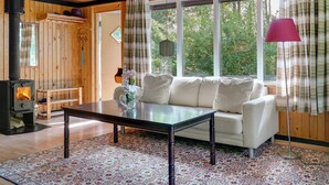 Ein gemütliches Blockhaus-Interieur mit einer Couch, einem Tisch, einem Kamin und großen Fenstern.