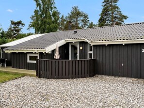 Een gebouw met twee verdiepingen, een donkere gevel, een overdekt terras en een oprit van grind.