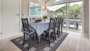 Een eethoek met een tafel gedekt voor vier personen, omringd door stoelen, een groot raam en uitzicht op groen.
