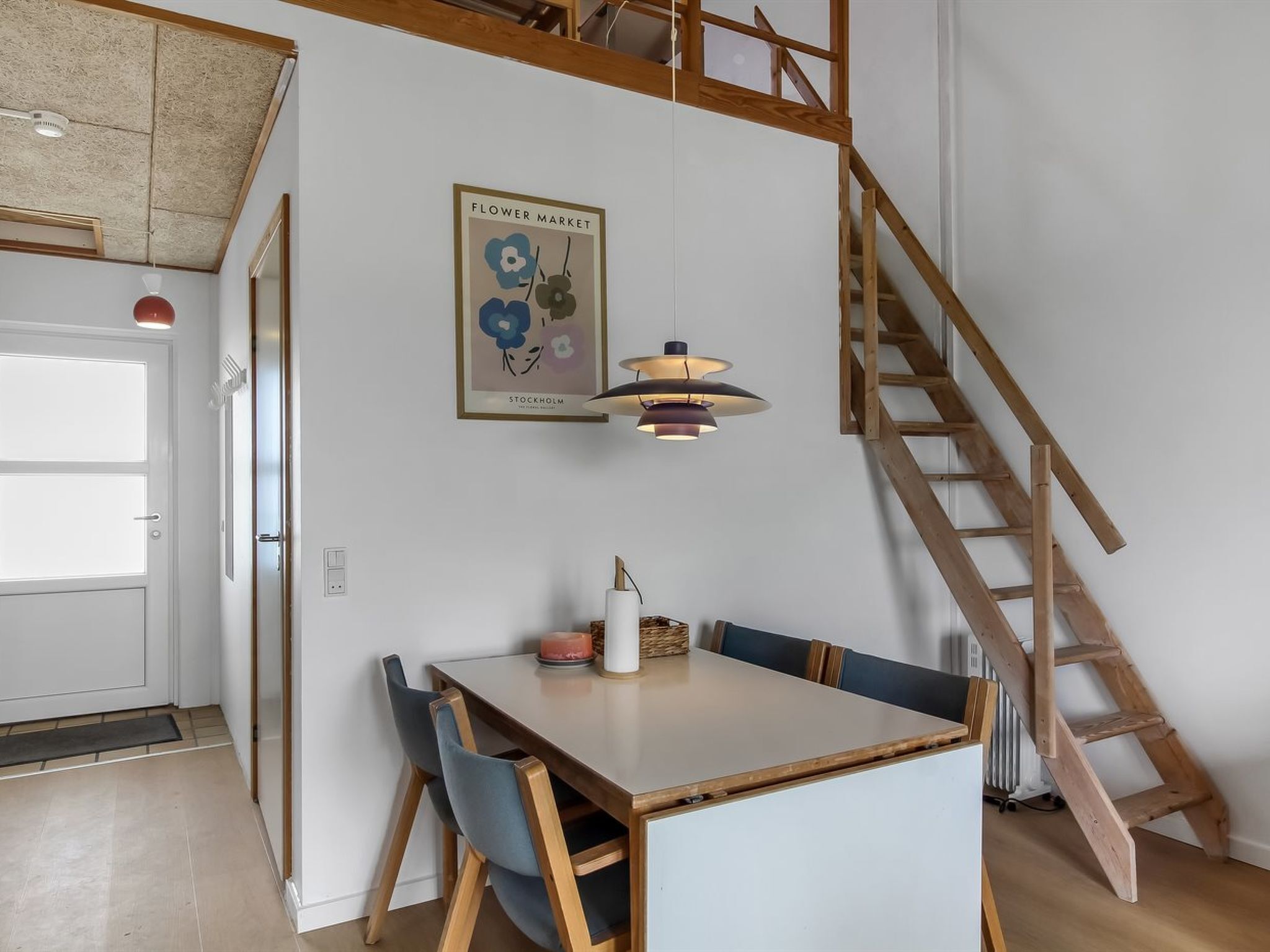 Un coin repas avec une table en bois, des chaises bleues, une suspension, une échelle en bois et un tableau encadré au mur.