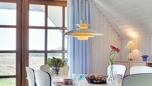 A dining area with a round table, chairs, a hanging light fixture, a vase with flowers, and a view through large windows. - "Vangja" - 700m to the fjord by Interhome (Hvide Sande)