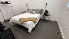 A neatly made bed with a white and beige blanket, two bedside tables with lamps, a coat rack, and a small desk with a chair. - 30 min to Chicago|2 TVs |Fireplace |W/D|Parking (Naperville)