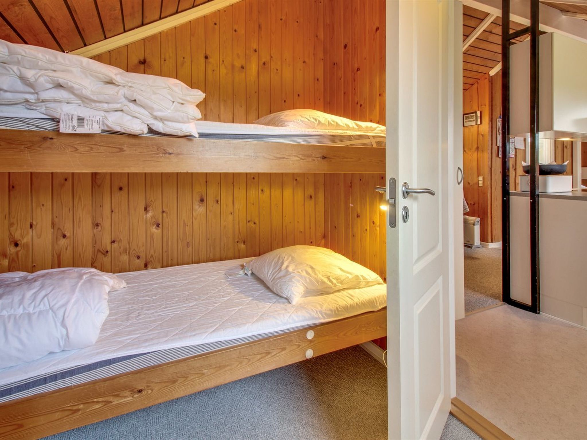 Een slaapkamer met stapelbedden, houten wanden en een witte deur.