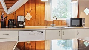 A kitchen with a dishwasher, coffee maker, microwave, and a window with curtains.