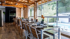 Un espace de repas moderne avec une longue table dressée pour six personnes, des chaises en bois et une vue sur une piscine, visible à travers de grandes fenêtres.
