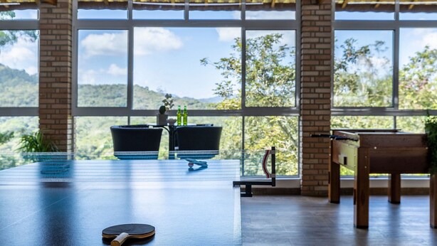 Une table de ping-pong dans une pièce dotée de grandes fenêtres, d’un mur en briques et d’un plafond en bois.