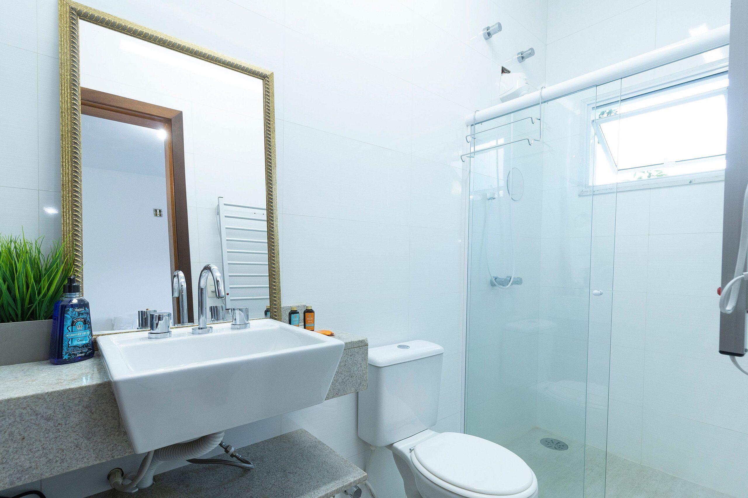 A bathroom with a white sink, a mirror with a gold frame, a toilet, and a glass-enclosed shower.