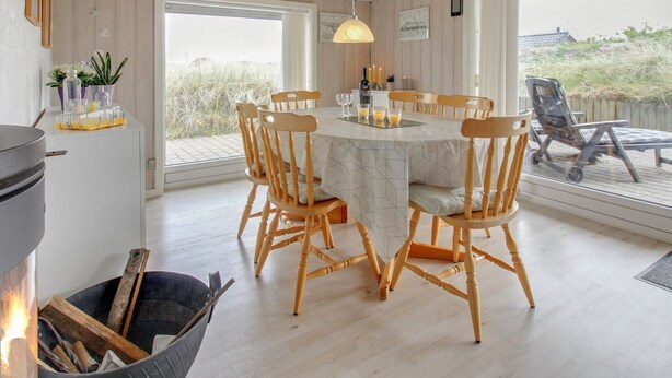 Un coin repas avec une table ronde, des chaises en bois, un luminaire suspendu et une vue dégagée sur l’extérieur grâce à une grande fenêtre.