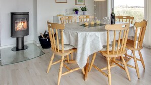 Un coin repas avec une table ronde, des chaises en bois, une table à plateau en verre, un poêle à bois noir et deux tableaux encadrés accrochés au mur.