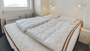 Un lit double avec une literie blanche, une fenêtre donnant sur un paysage agréable, une étagère avec des fleurs et un radiateur.