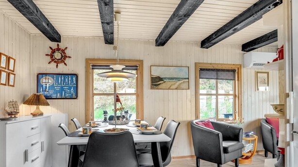 A dining area with a wooden table, black chairs, and a pendant light. There are windows with curtains, a wall clock, and a framed picture. - "Marite" - 200m from the sea by Interhome (Pandrup)