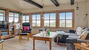 A cozy living room with a wooden table, a leather chair, a sofa, and large windows offering a view of the outdoors. - "Marite" - 200m from the sea by Interhome (Pandrup)