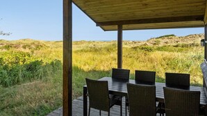 A covered outdoor seating area with a table and chairs, overlooking a grassy landscape with dunes. - "Marite" - 200m from the sea by Interhome (Pandrup)
