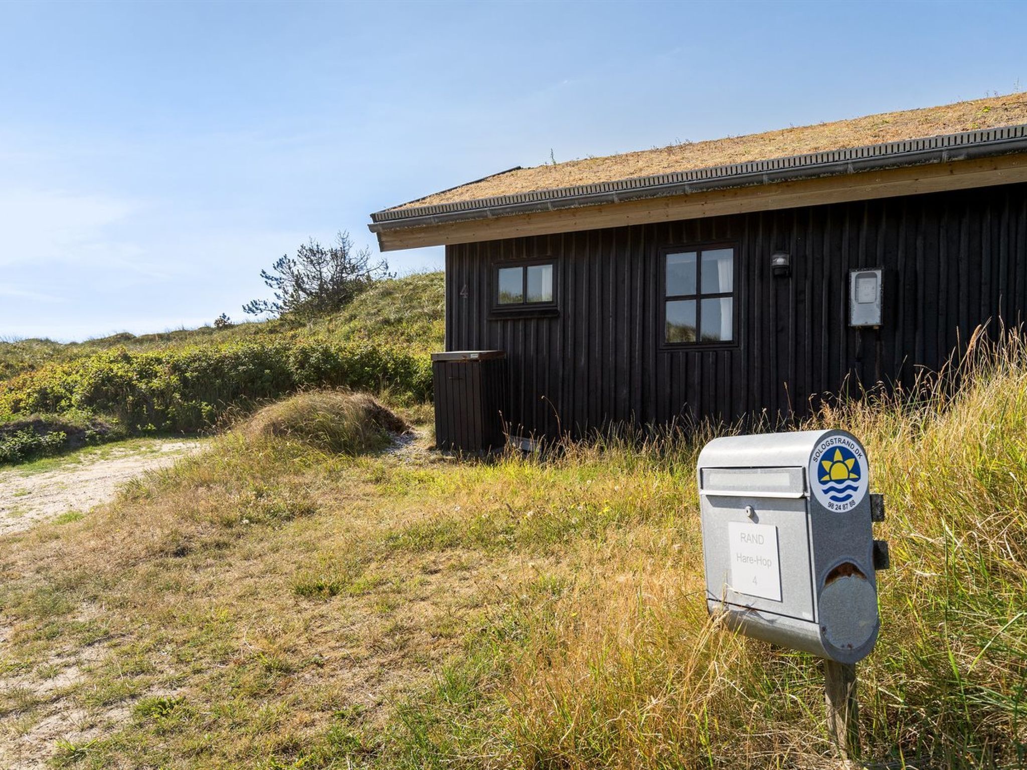 Un bâtiment en bois avec une boîte aux lettres métallique portant les inscriptions « SOLOSTRAND DK » et « RAND Hare-Hope 4 ».